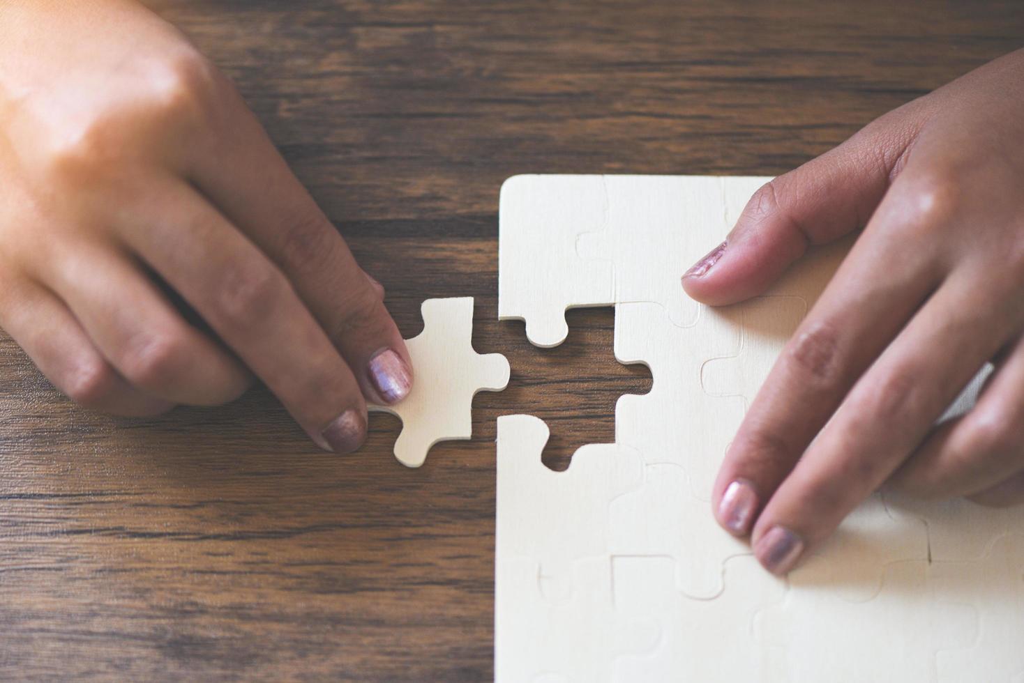 jigsaw puzzle with woman hand connecting jigsaw piece on wooden background Business solutions partnership success and strategy photo