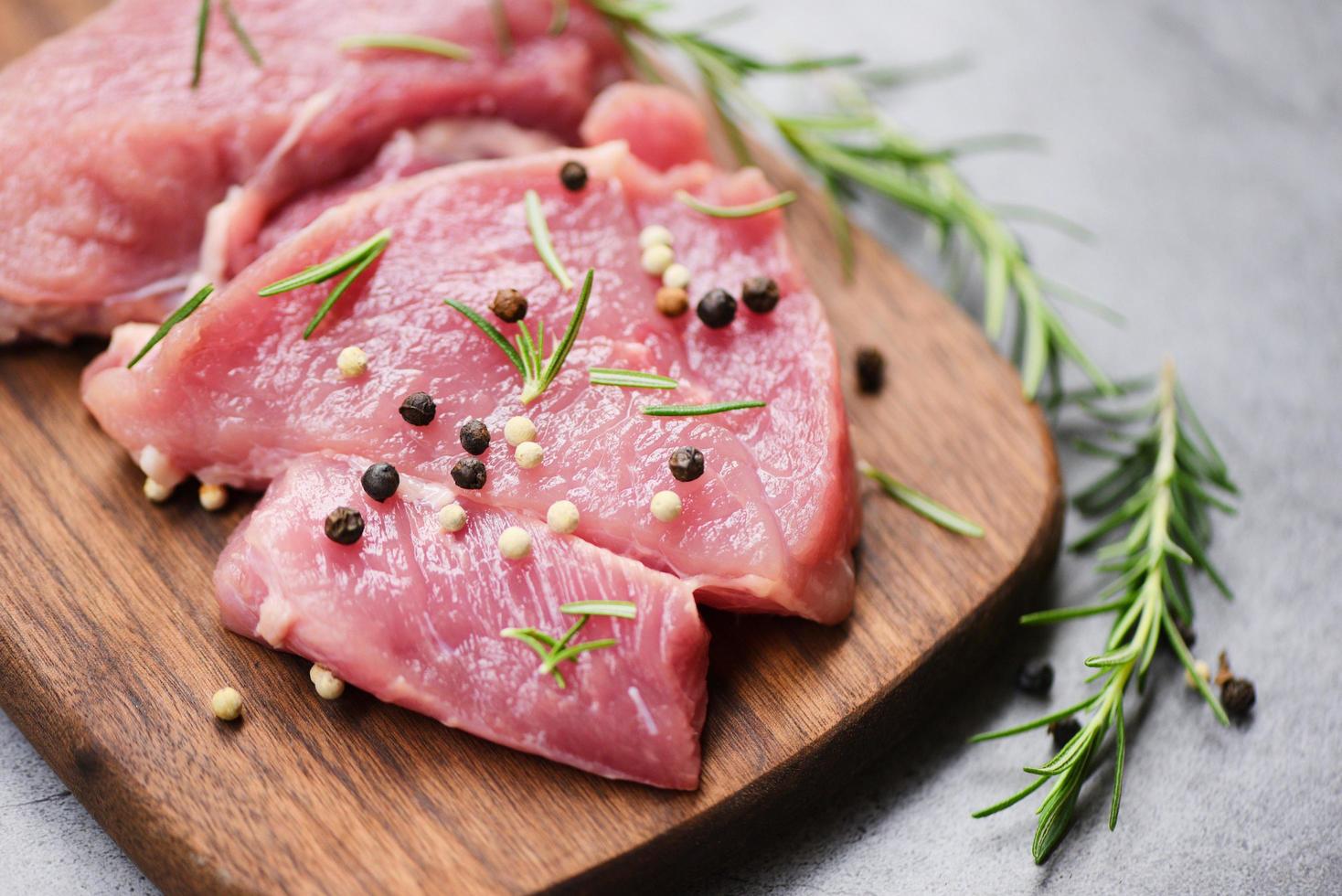 Raw pork meat on wooden cutting board on the kitchen table for cooking pork steak roasted or grilled with ingredients herb and spices Fresh pork photo