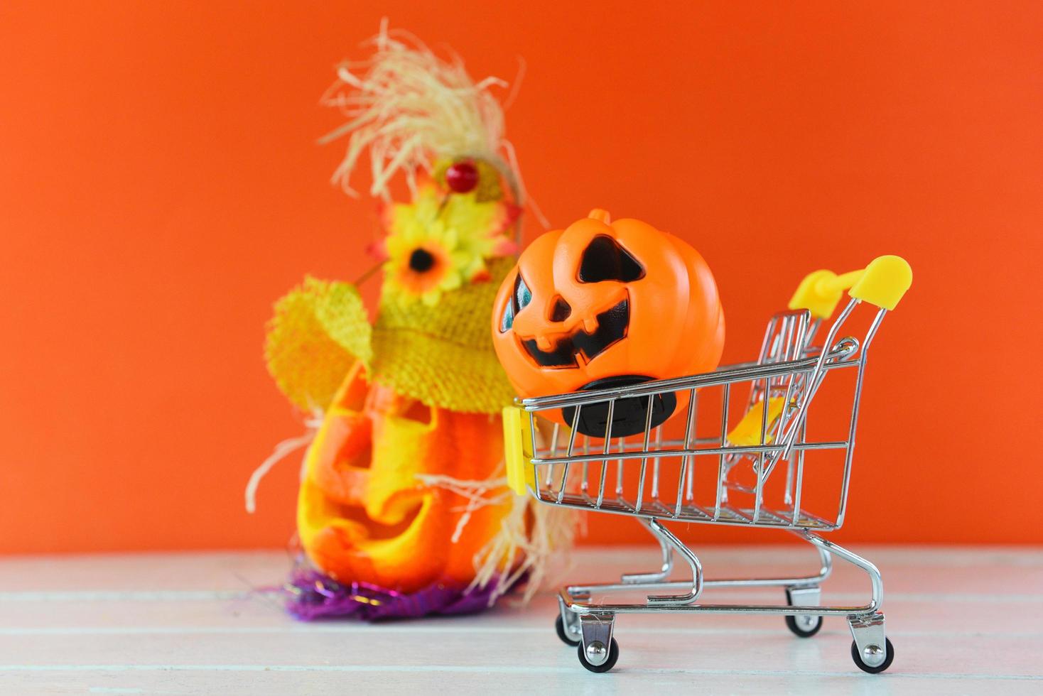 Halloween shopping holiday concept - accessories with pumpkin jack o lantern in a shopping cart on orange background photo