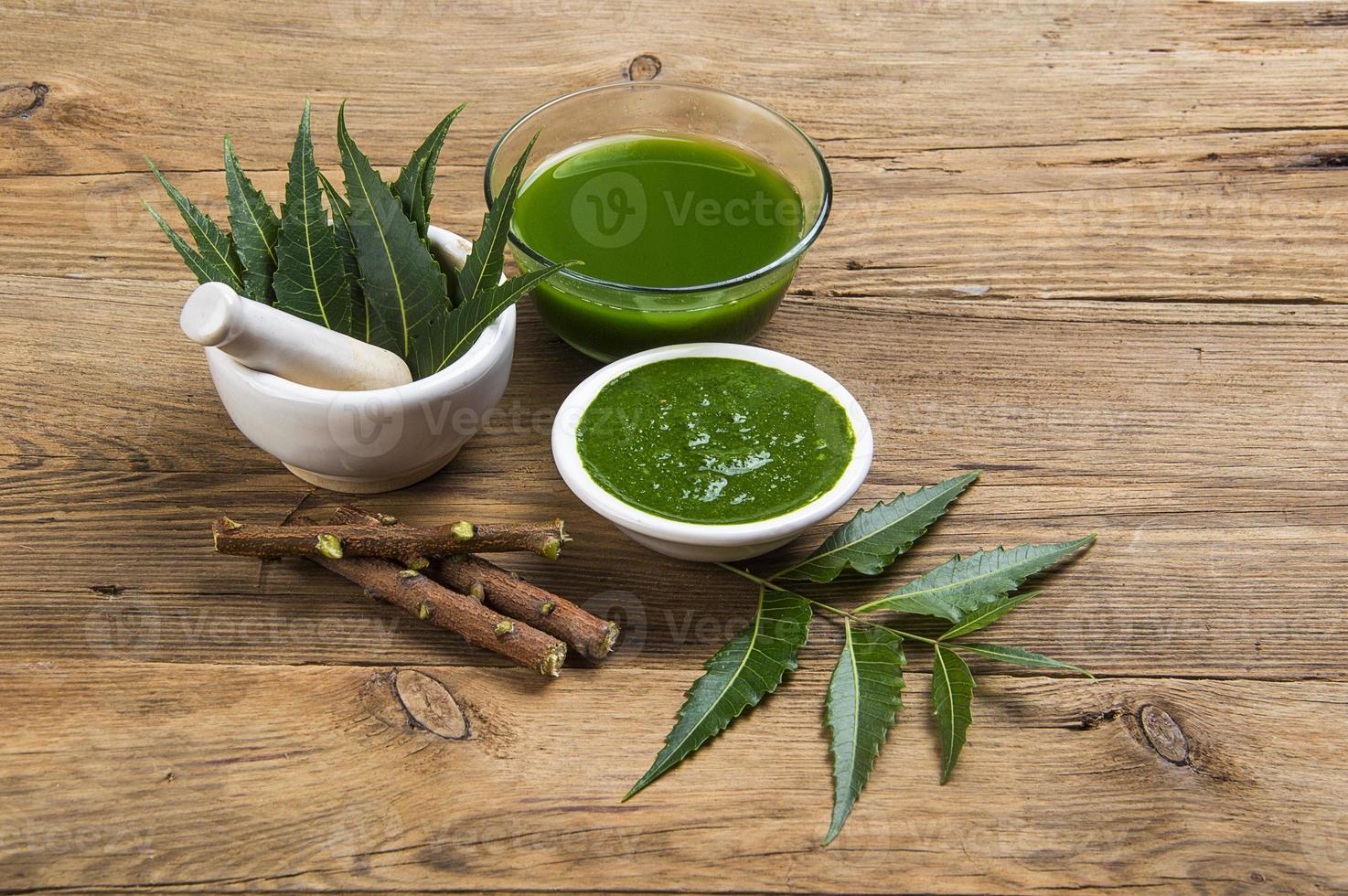 Medicinal Neem leaves in mortar and pestle with neem paste, juice and twigs on wooden background photo