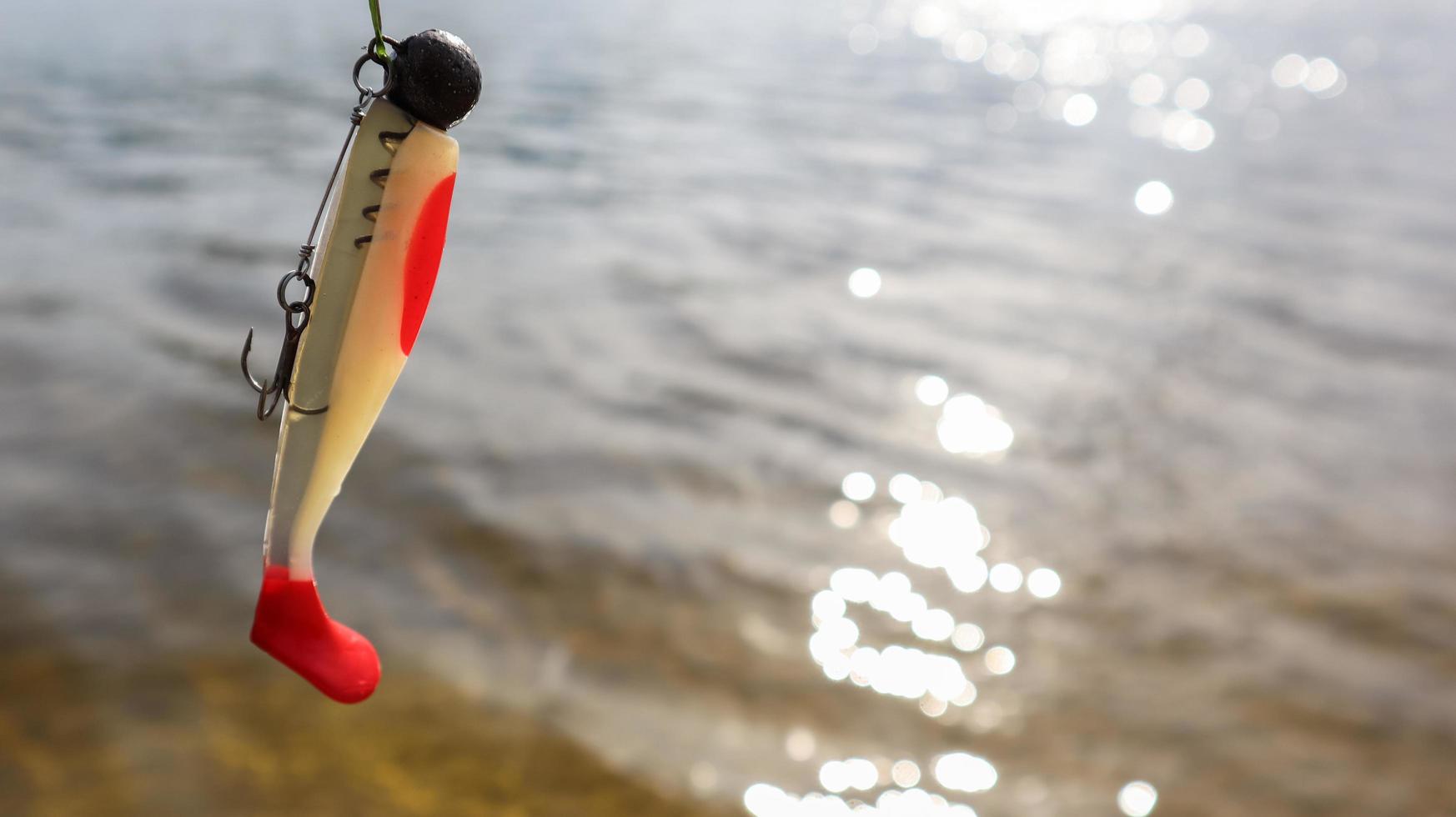 Ukraine, Kiev - June 2, 2020. Silicone fish wobblers hanging on a spinning rod, against the background of water. fishing lures for predatory fish. Copy space. Sport and hobbies photo