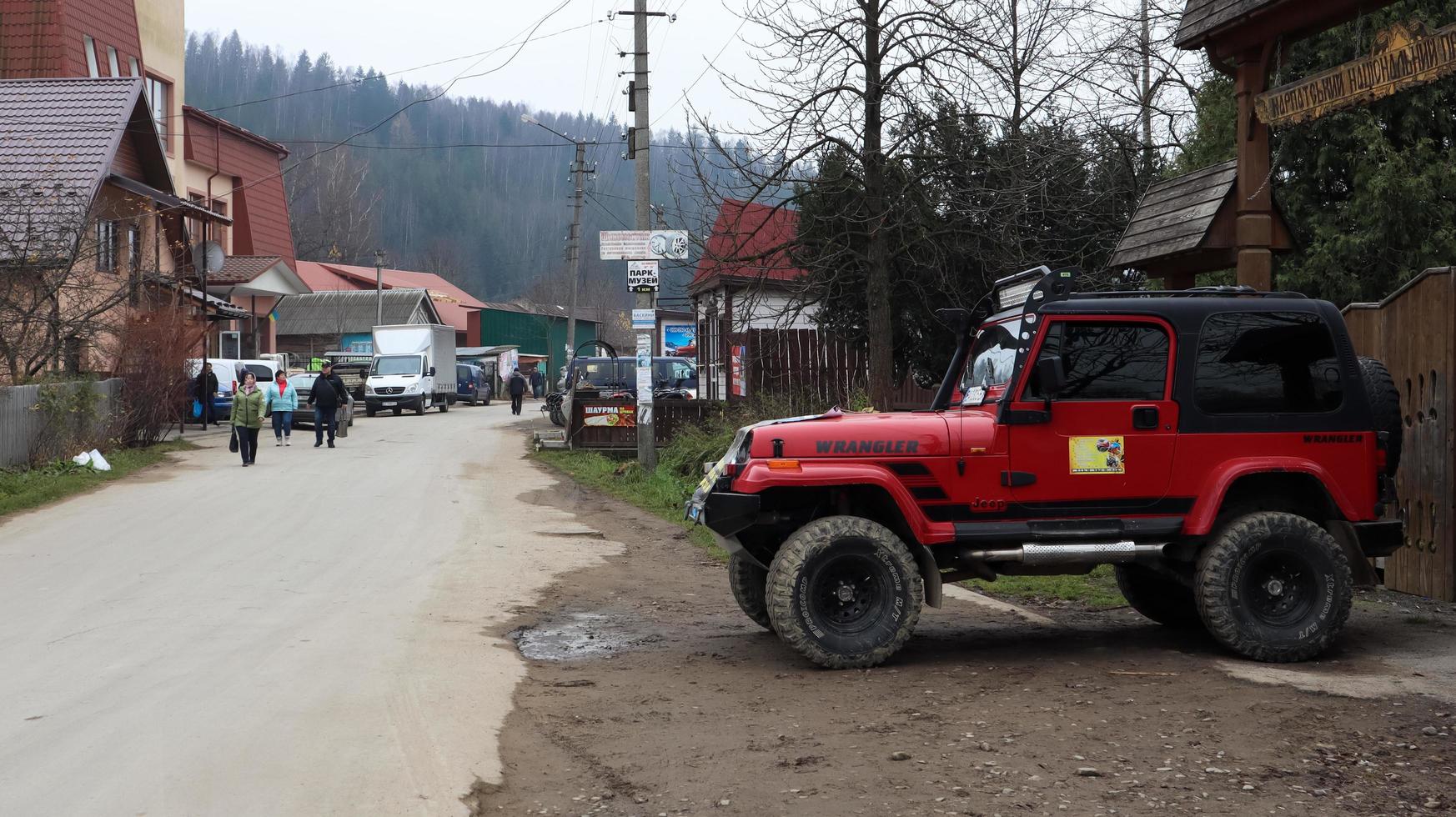 Ucrania, Yaremche - 20 de noviembre de 2019.Un jeep wrangler 4.0i v6 suv rojo está estacionado en una carretera rural cerca de una casa en un pequeño pueblo de los Cárpatos ucranianos. excursiones paseo en jeep de montaña. foto