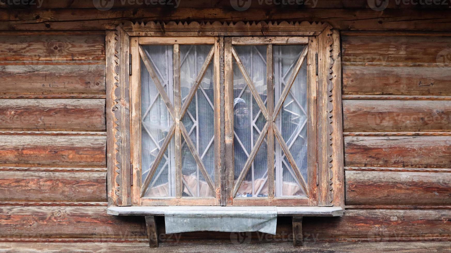 A small wooden window of a traditional old house. The window is closed and brown. An old window with a wooden frame from planks, which is part of an old rustic wooden house on a sunny summer day. photo