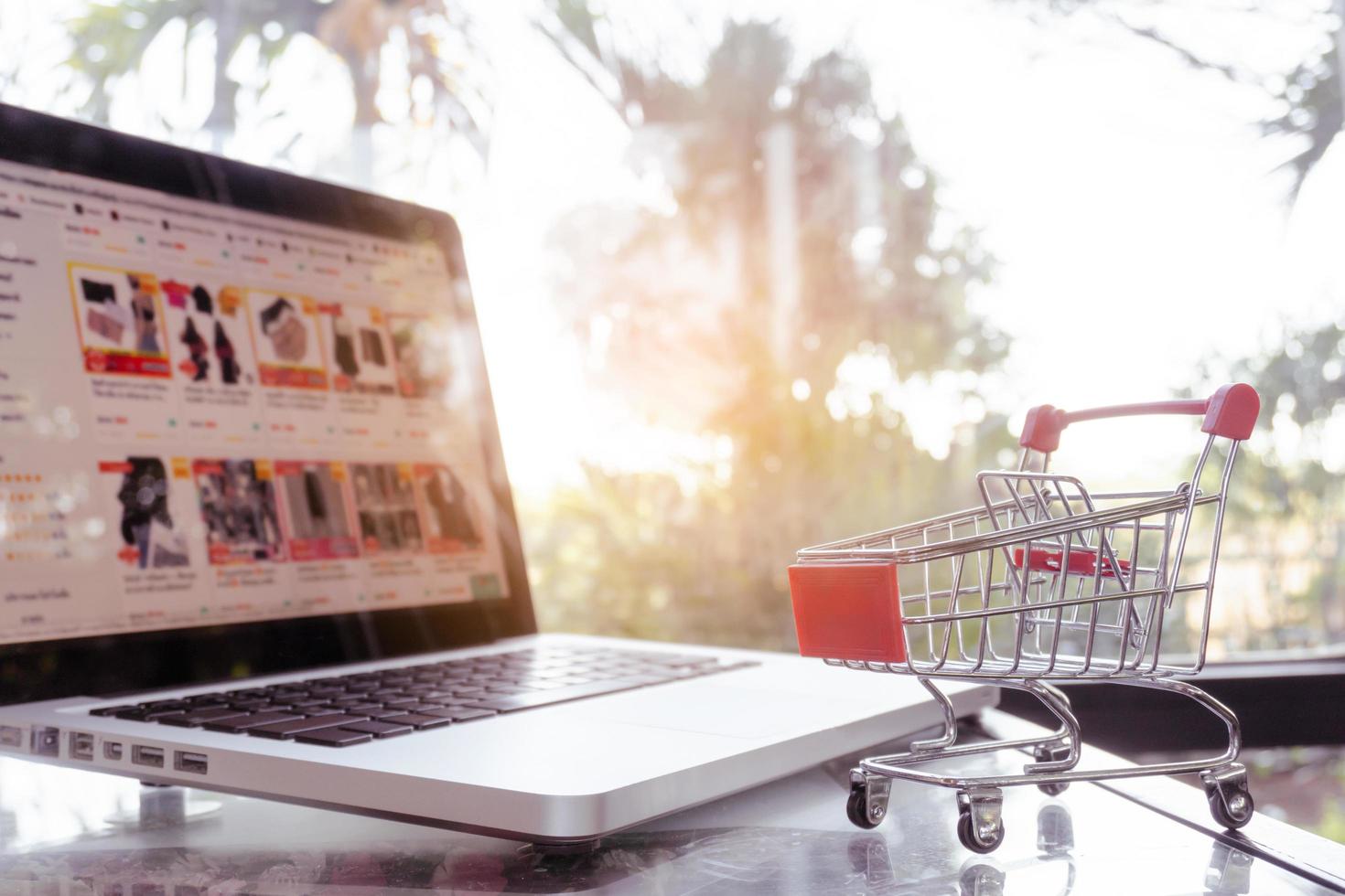 concepto de compras en línea: carrito de compras o carro y computadora portátil en la mesa foto