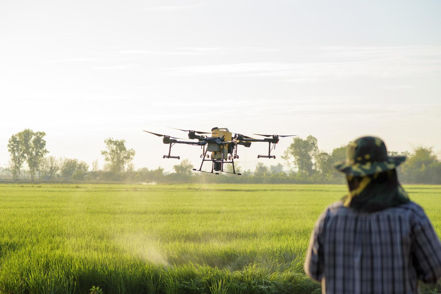 Young smart farmer controlling drone spraying fertilizer and pesticide over farmland,High technology innovations and smart farming photo