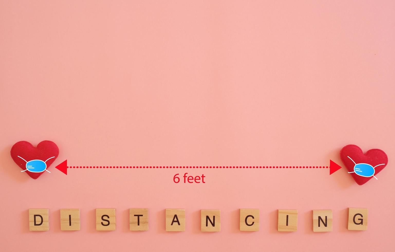 Social Distancing between two hearts in a protective antivirus mask with arrow and 6 feet distance, letter words of DISTANCING on pastel light pink background. Valentines Day during the coronavirus. photo