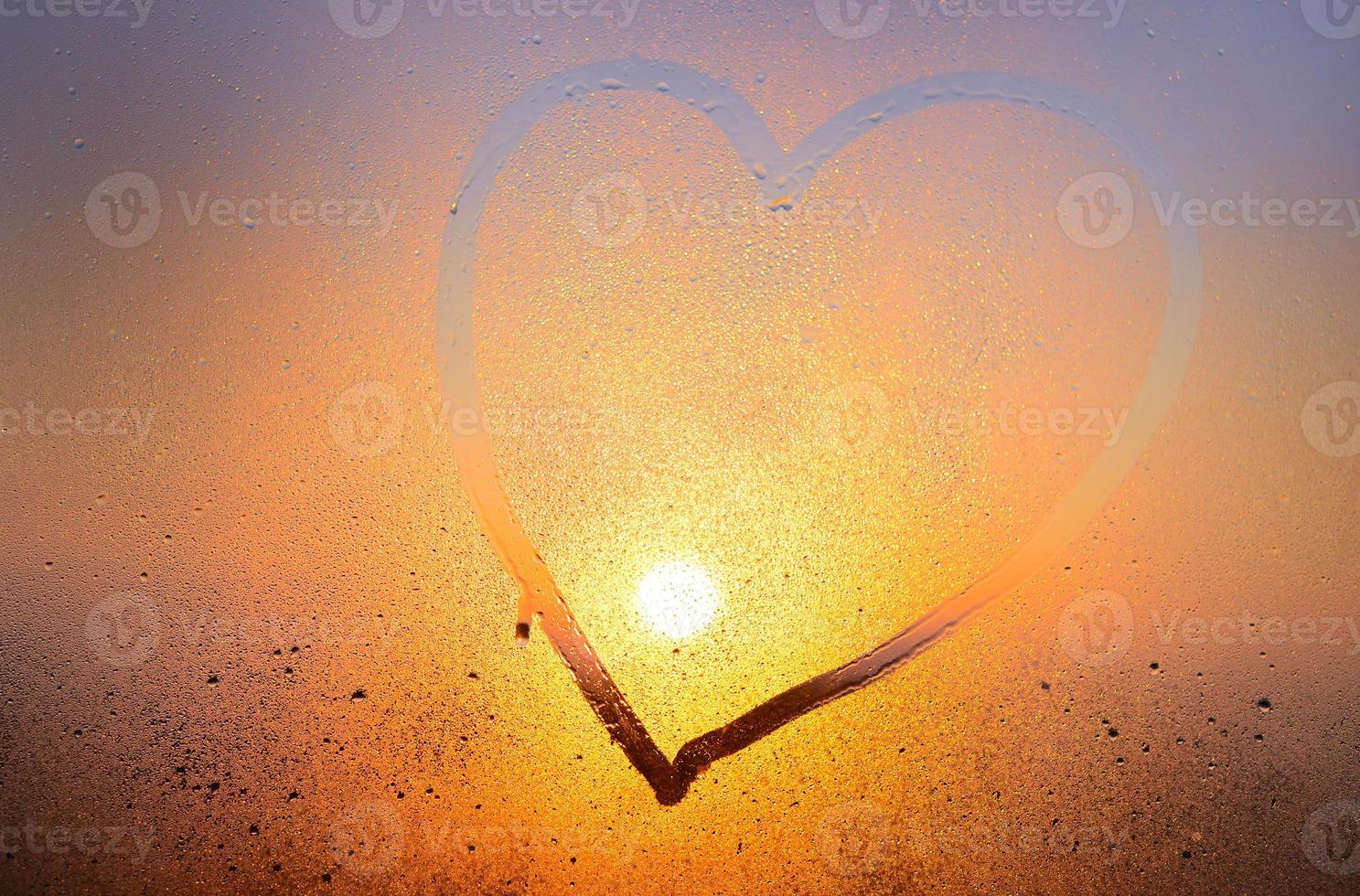 Shape of heart painted on fogged glass of window. Drawing of a heart on window, blurred background photo