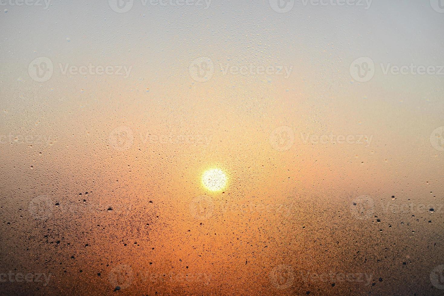 ventana de vidrio empañado con gotas de lluvia, fondo borroso. vista de la ciudad y luz del sol a través del vidrio empañado foto