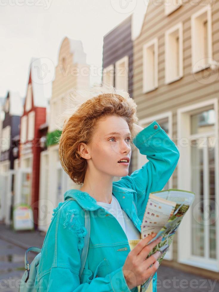 Portrait of redhead young woman in straw hat and with travel bag with paper map travel over West Europe. Travel and lifestyle photo