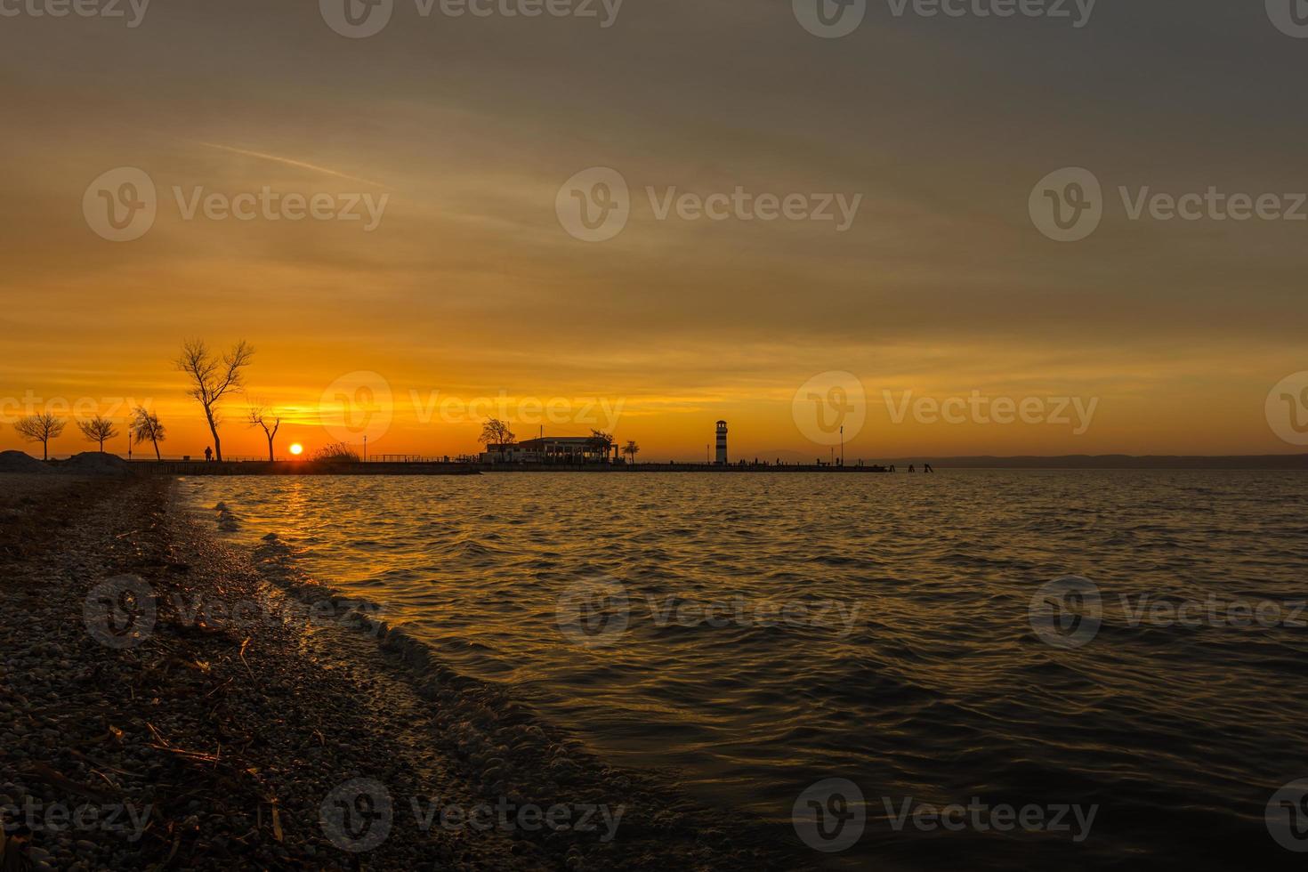 embarcadero con faro y olas en el lago al atardecer foto