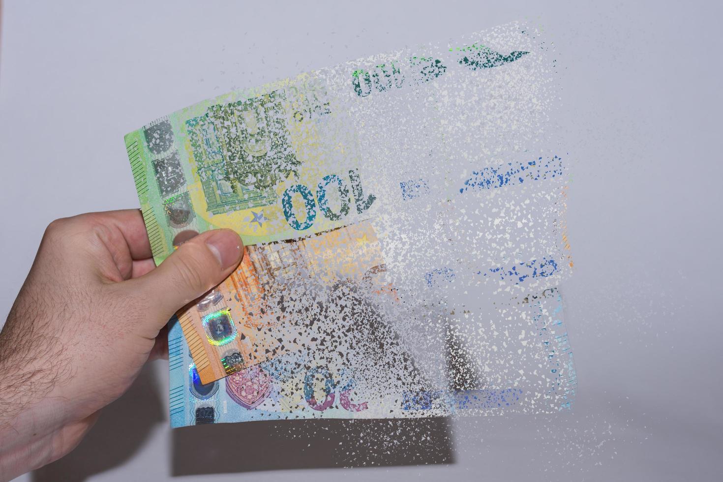 three euro bank note held in one hand decomposes and dissolves with gray photo