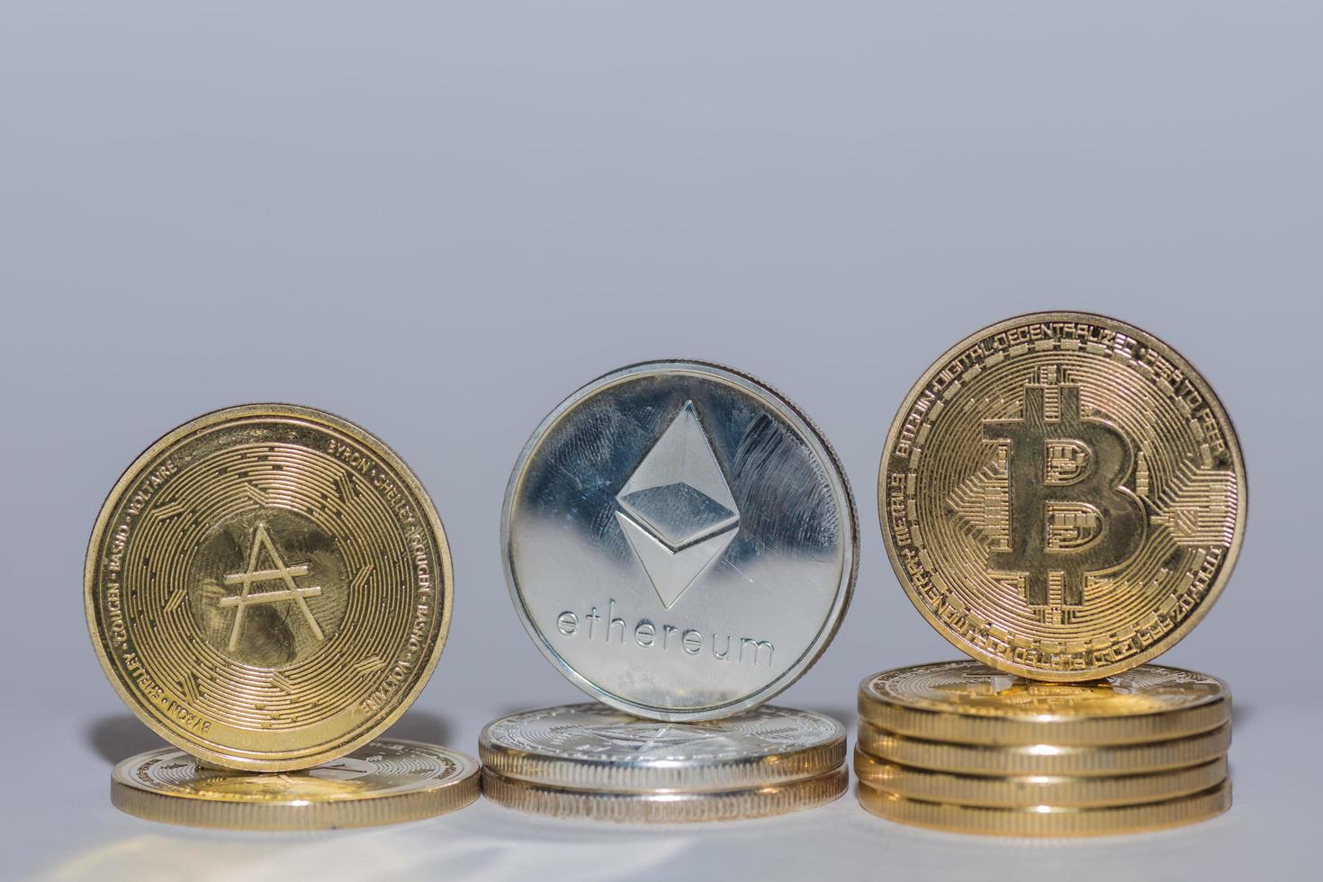 valiosas monedas criptográficas bitcoin ether y ada en una fila con fondo gris de cerca foto