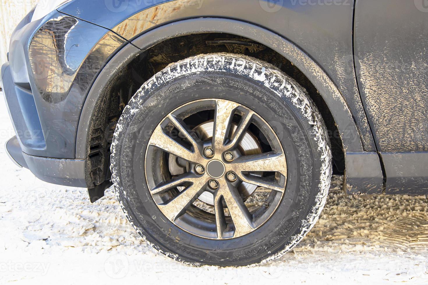 la rueda de un coche sucio sobre un fondo de nieve en una soleada mañana de invierno. foto
