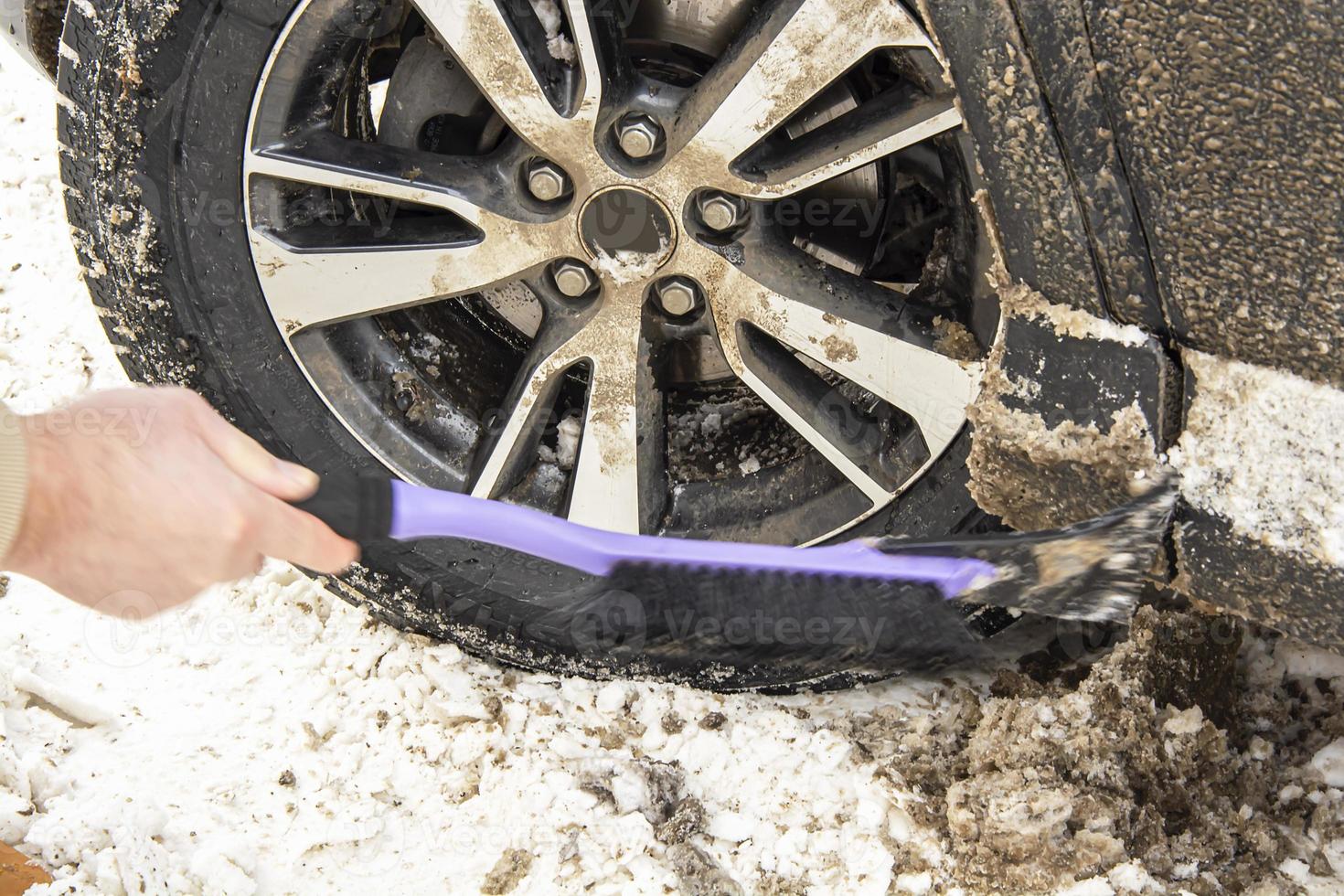 Cleaning a dirty car wheel with a brush scraper from dirt and snow on a sunny frosty winter morning. photo