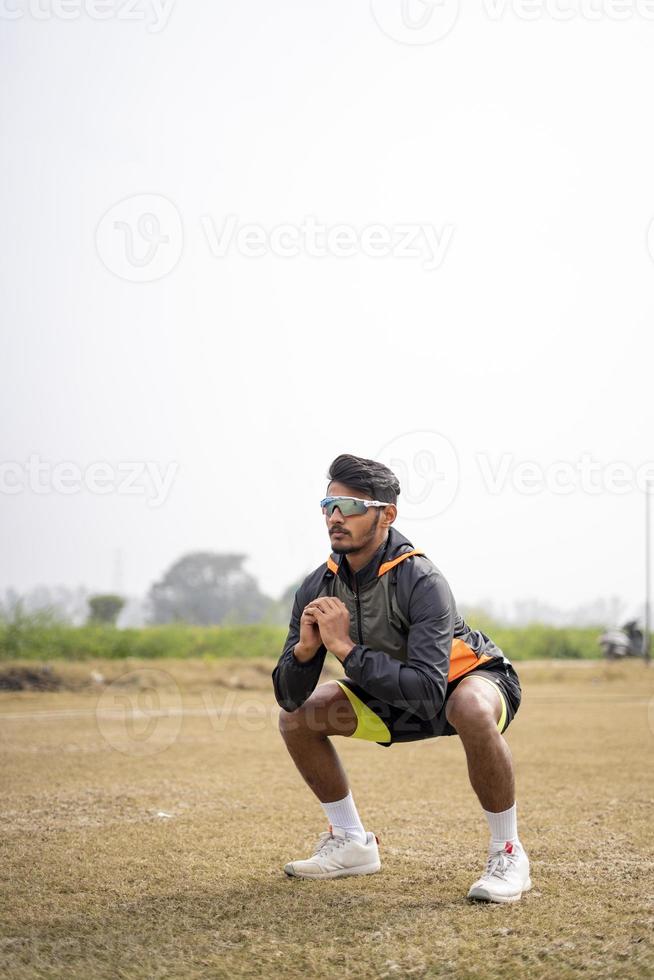 joven deportista indio haciendo sentadillas en el campo. concepto de estilo de vida saludable y deportivo. foto