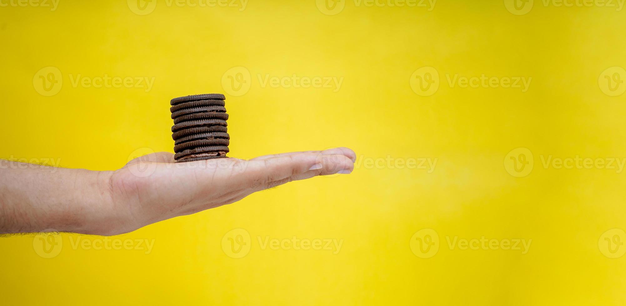 manos sosteniendo galletas de chocolate sobre un fondo amarillo con espacio para copiar foto