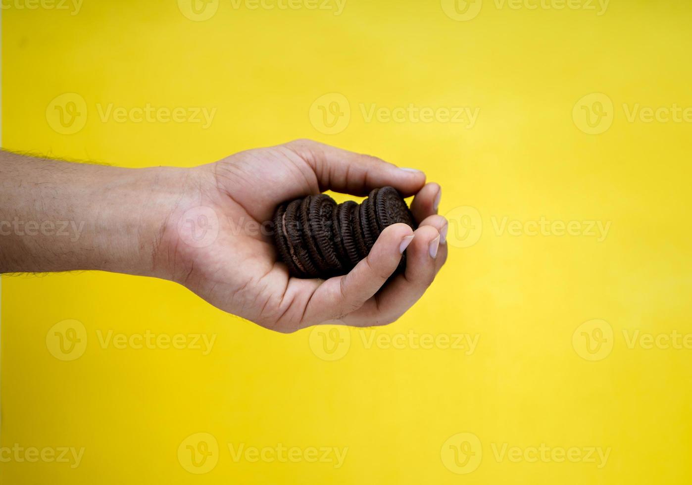 manos sosteniendo galletas de chocolate sobre un fondo amarillo con espacio para copiar foto