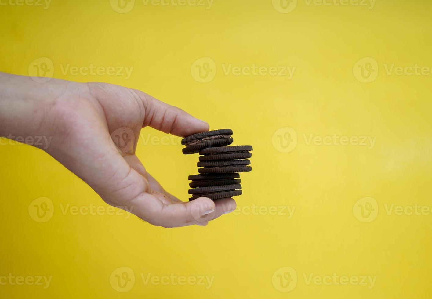 manos sosteniendo galletas de chocolate sobre un fondo amarillo con espacio para copiar foto