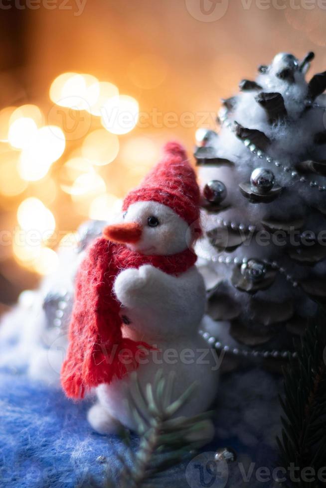 composición de año nuevo con muñeco de nieve hecho a mano con bufanda y sombrero de punto rojo. foto