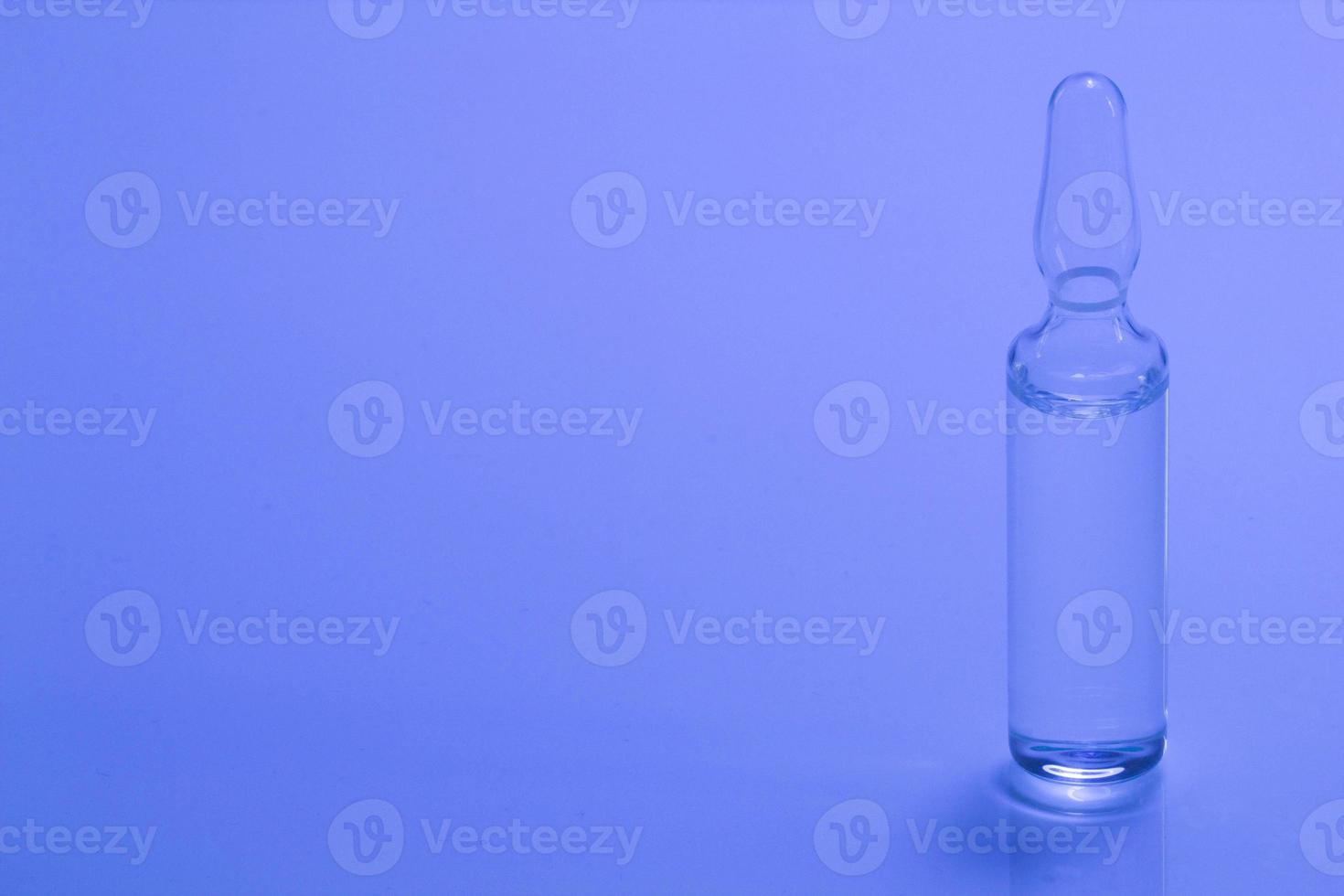 Medical ampoule on a blue background. Glass ampoule for injection with medicine on the table. Concept medicines and disease treatment. Pharmacology, cosmetology, science. Copy space for text. Close-up photo