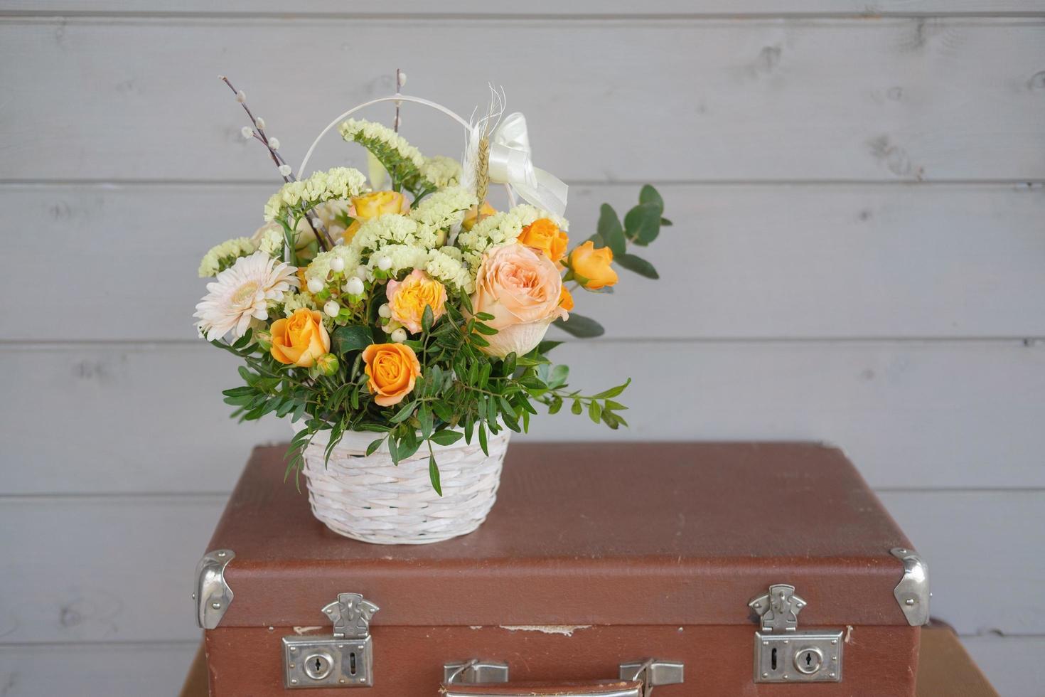 a beautiful bouquet of fresh flowers in a basket on a vintage suitcase on a gray wall background photo