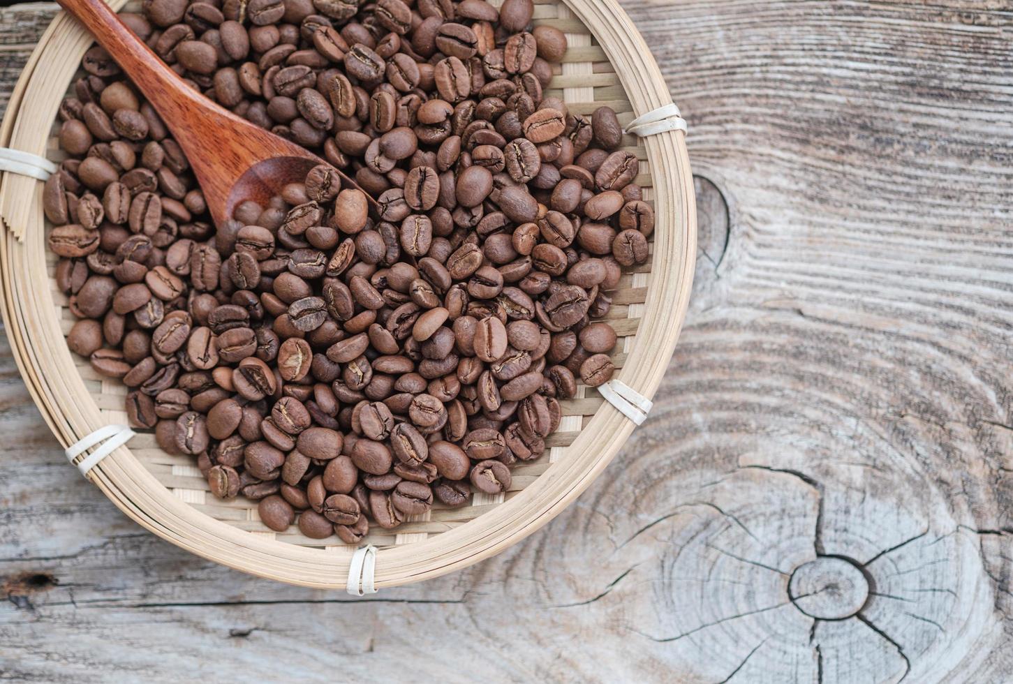 granos de café en un plato de bambú en el fondo de un viejo tablero foto