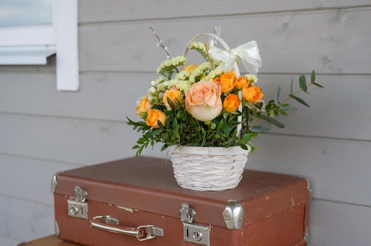 a beautiful bouquet of fresh flowers in a basket on a vintage suitcase on a gray wall background photo