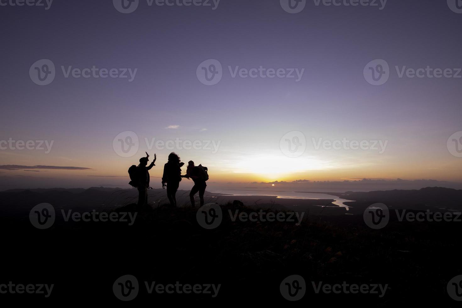 tres siluetas de personas al amanecer en la cima de una montaña foto