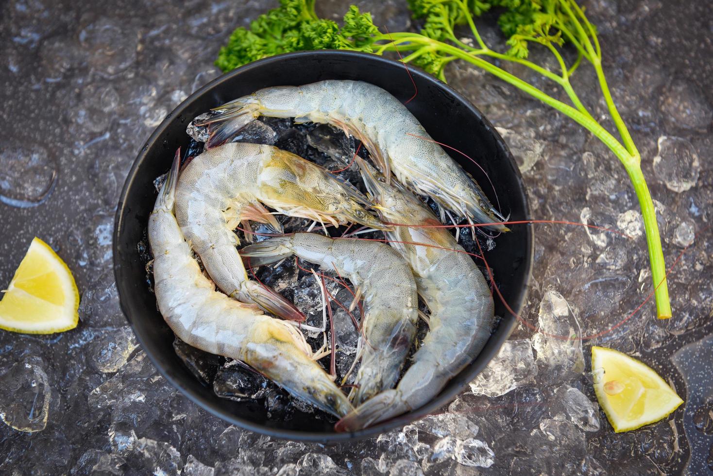 raw shrimps on bowl, fresh shrimp prawns for cooking food with spices lemon parsley vegetable on dark background in the seafood restaurant, top view photo