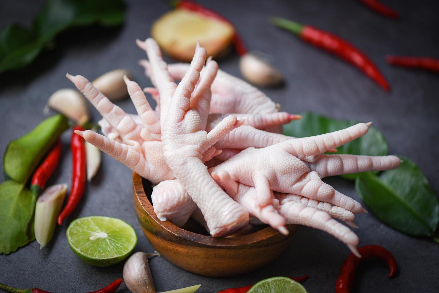 patas de pollo en un tazón de madera con hierbas y especias limón chile ajo hojas de lima kaffir hierba de limón, patas de pollo crudas frescas para sopa de comida cocida en el fondo de la cocina de mesa oscura foto