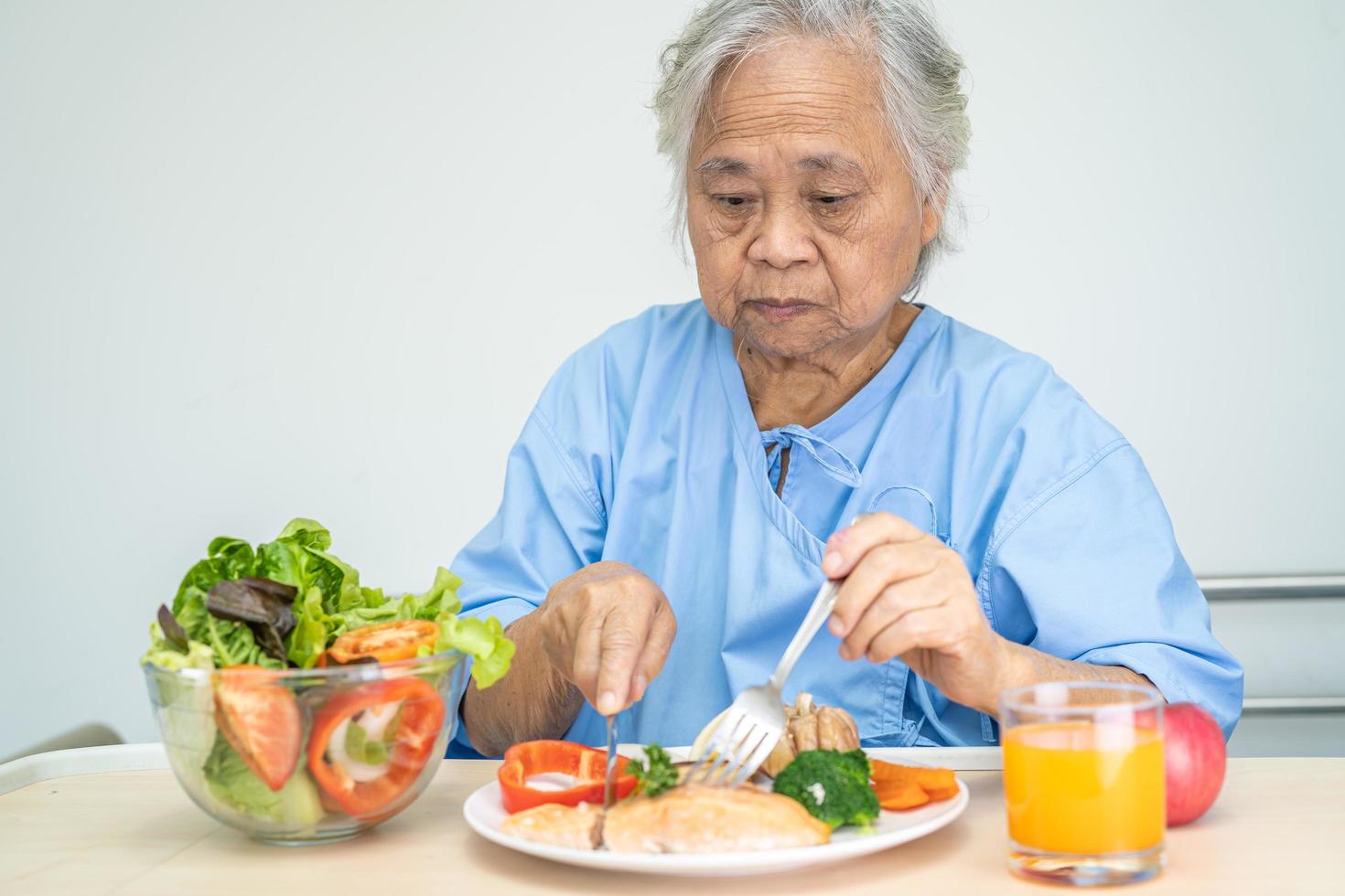 Paciente asiática mayor o anciana anciana desayunando filete de salmón con comida saludable vegetal mientras está sentada y hambrienta en la cama en el hospital. foto