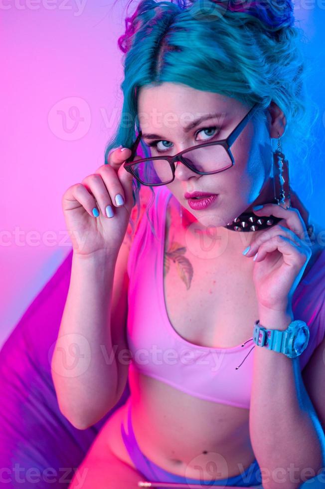 a sexy woman in a bright swimsuit with blue hair and glasses is sitting on a chair. photo