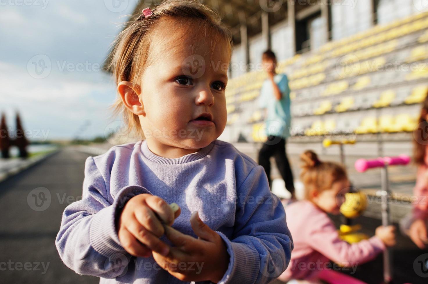 Cierra a una pequeña niña con traje deportivo morado. la familia deportiva pasa tiempo libre al aire libre con scooters y patines. foto