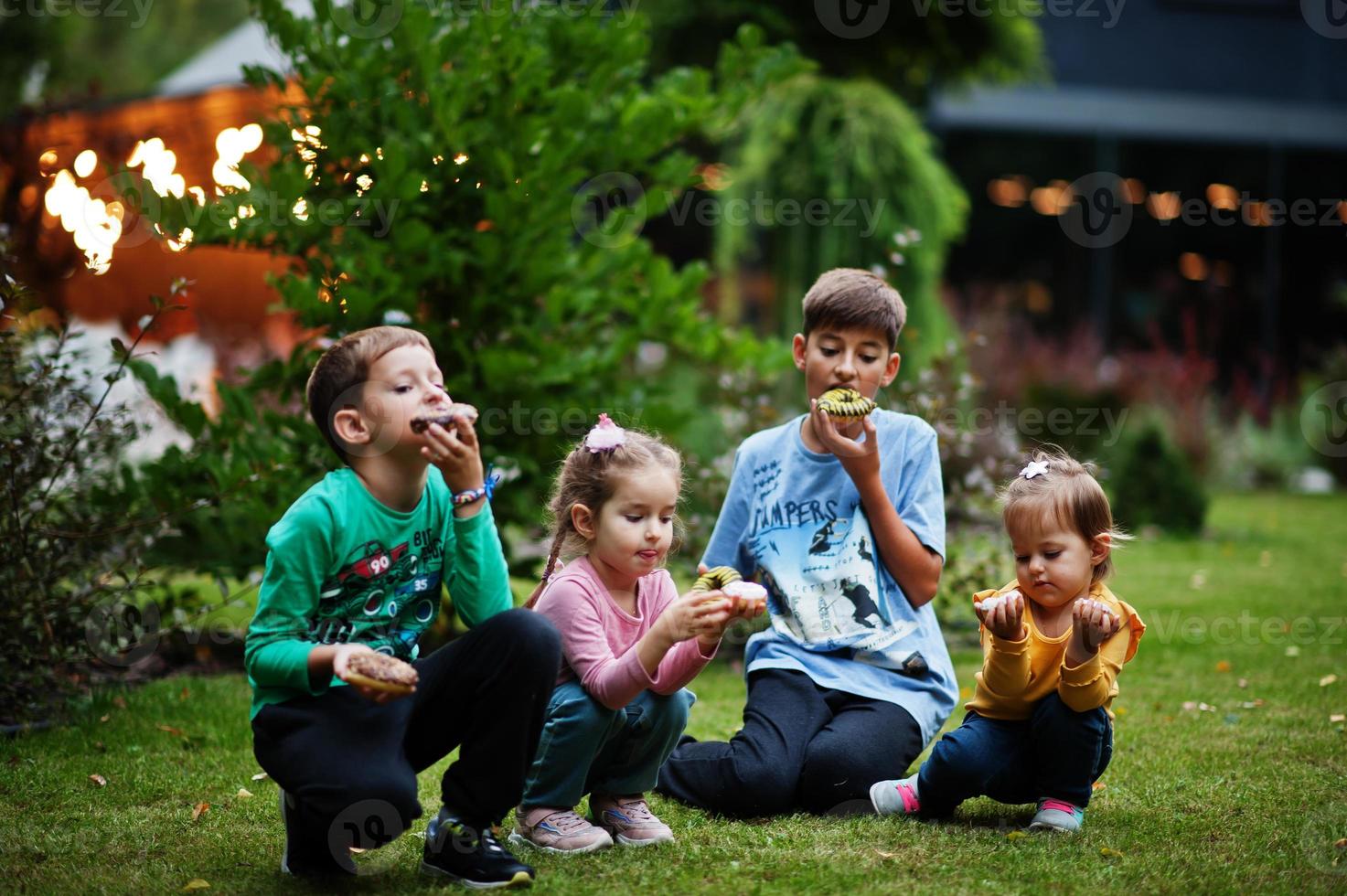 Four kids with doughnuts at evening yard. Tasty yummy donut food. photo