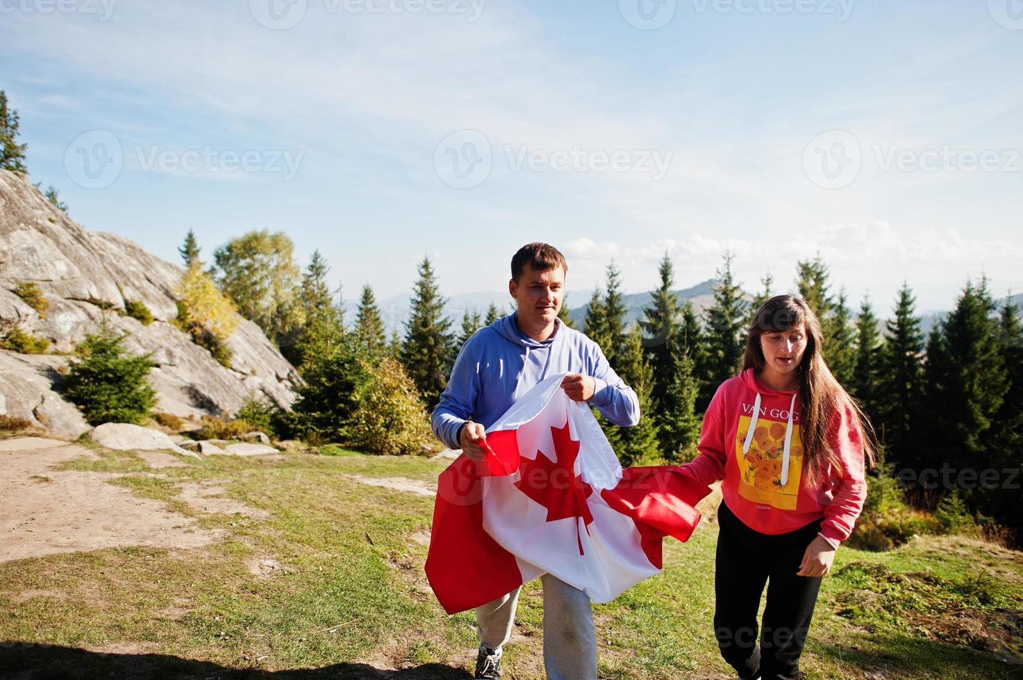 Happy Canada Day. Couple with large Canadian flag celebration in mountains. photo
