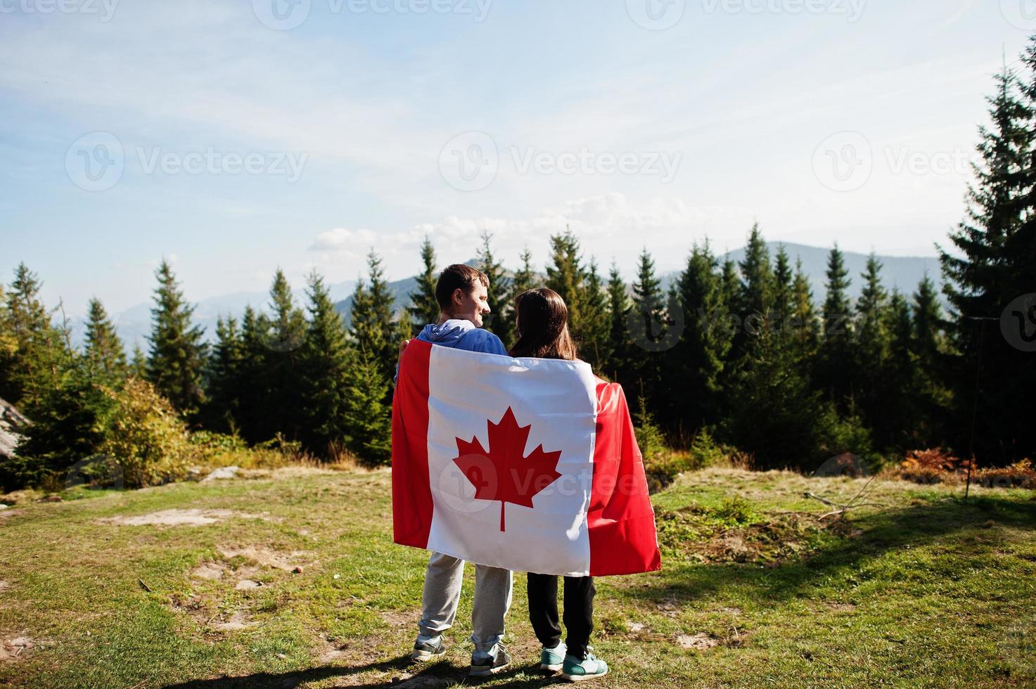 Happy Canada Day. Couple with large Canadian flag celebration in mountains. photo