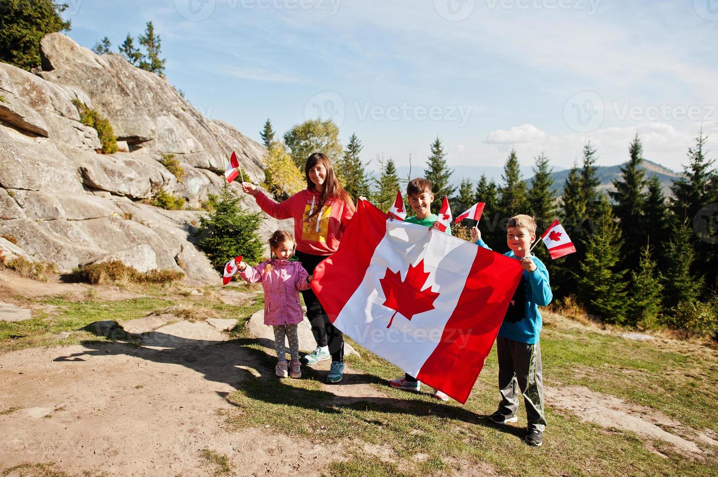 Happy Canada Day. Family of mother with three kids hold large Canadian flag celebration in mountains. photo