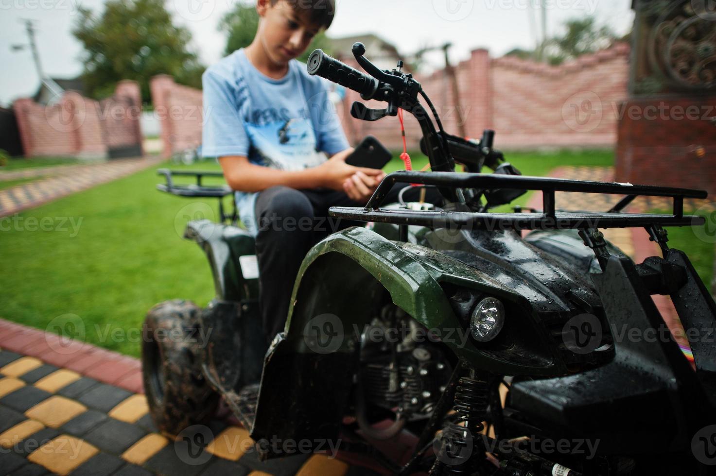 niño en cuatriciclo atv de cuatro ruedas con teléfono móvil. foto