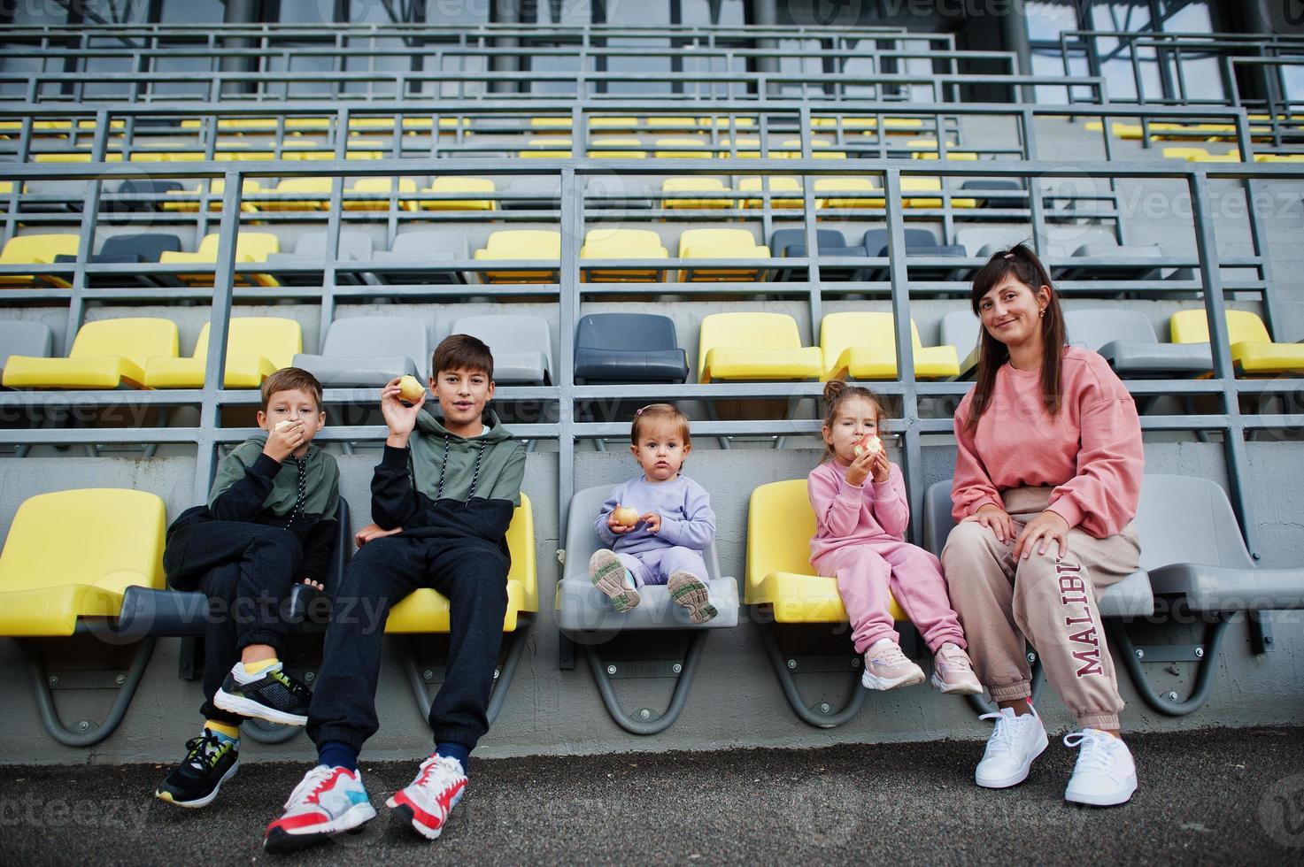 joven madre elegante con cuatro hijos sentados en sillas en el estadio. la familia pasa tiempo libre al aire libre. foto