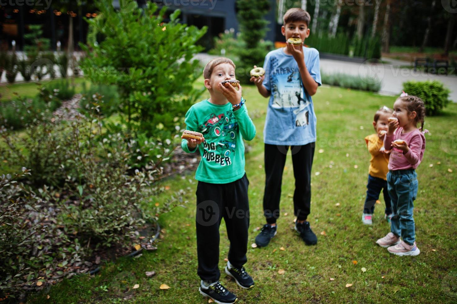 Four kids with doughnuts at evening yard. Tasty yummy donut food. photo
