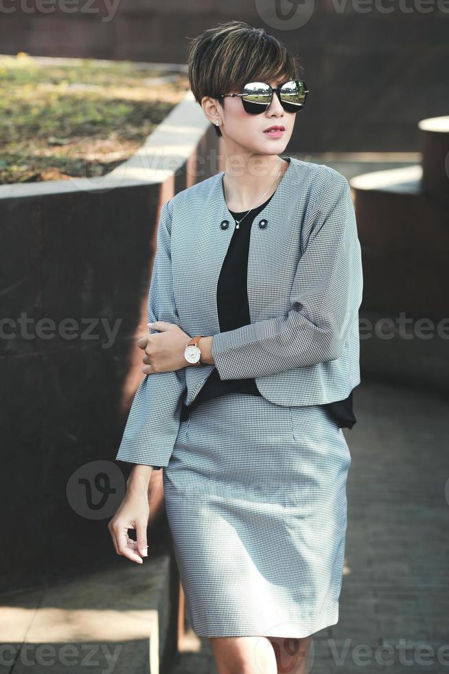 Fashion short hair business woman in sunglasses at the park. Stylish model in gray blazer and skirt photo