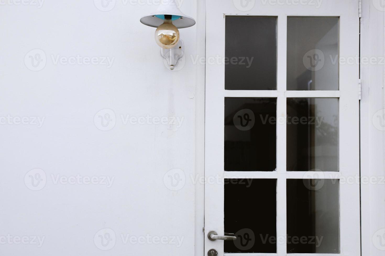 Minimalist white exterior house design with white entrance door with glass and hanging bulb lamp photo