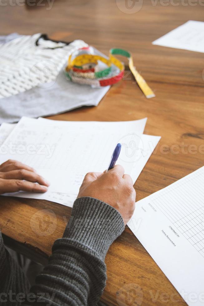 Closeup of a young man fashion designer writing on paperwork. On process of creating new clothes collection. photo