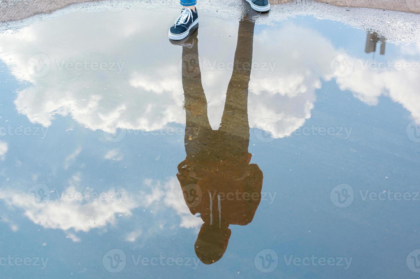 Reflection in water of man with casual style standing in bright blue sky photo