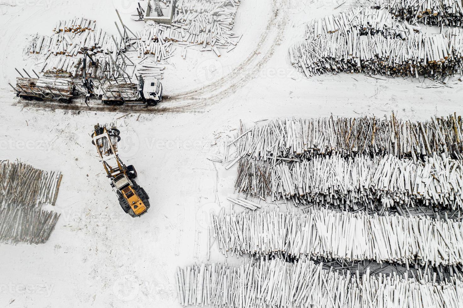 Loader loads logs into the truck stacked in piles covered with snow top view photo