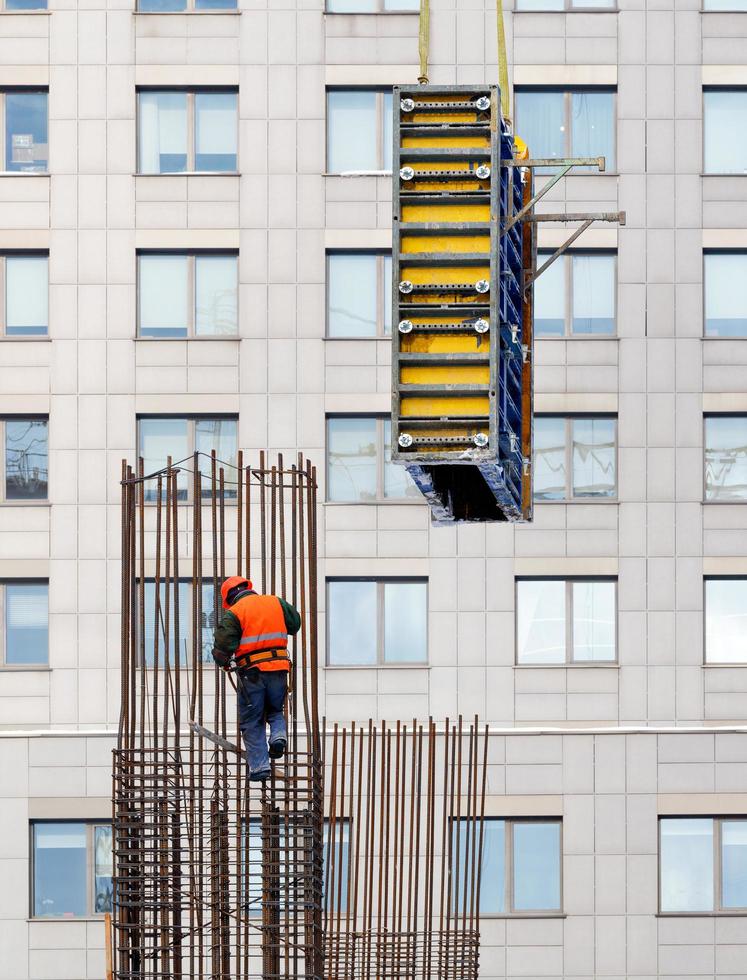 16.02.2021. kiev Ucrania. un constructor que lleva un chaleco naranja brillante y un casco de seguridad instala el encofrado en un marco de acero para el posterior vertido de hormigón. foto