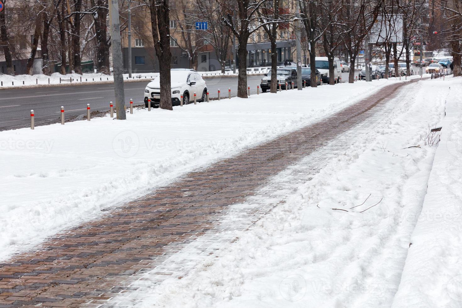 The sidewalk cleared of snow runs along the carriageway of the city street. photo
