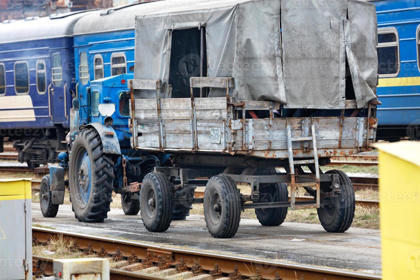 An old tractor with a wooden trailer and a booth rides on a railway platform. photo