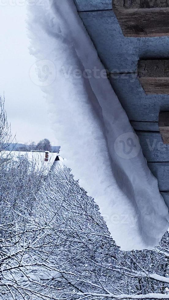 Danger. Snow hangs from the roof. Snow landslide. photo