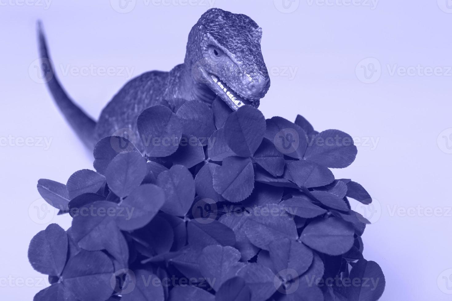 St. Patrick's Day happy dinosaur, a bouquet of clover in a bucket and gold coins on a very peri background. Closeup copy space photo